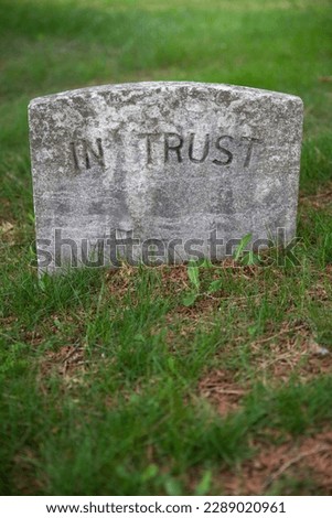 Vertical image of an ancient grave stone in a green grassy cemetery. Tombstone reads only -- In Trust. No people, foreground copy space.