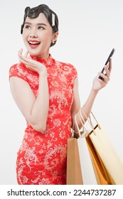Vertical image of attractive gorgeous Asian woman wearing qi pao, cheongsam looking sideway holding shopping bags and phone exciting for sale event this lunar Chinese New Year season - Shutterstock ID 2244737287