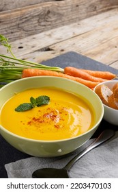 Vertical Image Of Bowl Of Carrot Soup With Garnish, Carrots And Sliced Bread On Wood, Copy Space. Tasty Home Cooked Food And Healthy Eating.