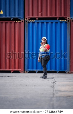 Vertical image Cargo logistics scene featuring African female worker using walkie talkie to supervise container operations, symbolizing import export business and freight transportation control.