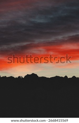 Vertical image of a dramatic sunset sky with deep red and dark gray clouds over a mountain silhouette. A moody and visually powerful scene ideal for posters, backgrounds, or emotional nature content.