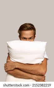 Vertical Image Of Handsome Angry Caucasian Man With Furrowed Brow, Hiding Behind White Rectangular Pillow, Squeezing It With Hands, Frowning, Getting Mad Of Having Problems With Sleep