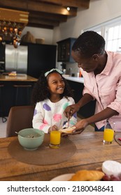 Vertical Image Of Happy African American Girl Eating Breakfast With Mother. Family And Spending Quality Time Together Concept.