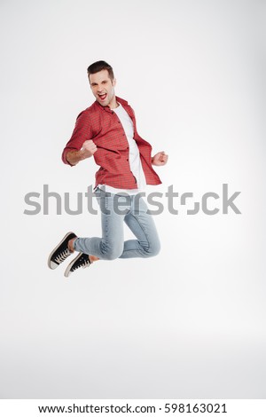 Vertical image of happy man in shirt and jeans which jumping in studio. Full length portrait over white background