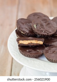 Vertical Image Of Homemade Peanut Butter Cups Piled On A White Platter, One Cup Cut In Half.Wooden Background. Close Up.