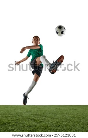 Vertical image low angle view of boy, soccer player in motion during training session, competing for victory, kicking ball in a jump against white background. Concept of sport, education, competition