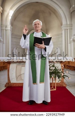 Vertical image of priest in formalwear reading Bible and blessing people during religious ceremony in church