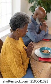 Vertical Image Of Senior African American Couple Praying Before Meal. Family And Spending Quality Time Together Concept.