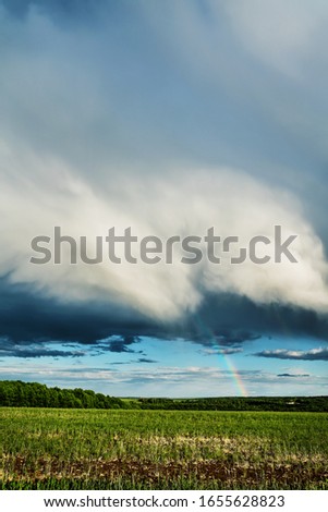 Vertical image shows rainclouds over a field with rainbow