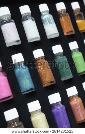 Vertical image of small bottles with multicolored sparkles glistering. Multicolored decorative elements for nail design. Tinsel for decoration of clothes, makeup. Selective focus.
