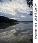 Vertical Image Of Sun Breaking Through Cloudy Sky Over Lake With Morning Mist Over Water And Tree Lined Horizon Outdoors