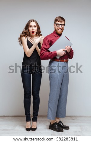 Vertical image of Surprised woman with Male nerd in eyeglasses which holding laptop. Isolated gray background
