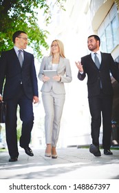 Vertical Image Of Three Business Partners Talking While Walking Down Modern Street 