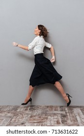 Vertical Image Of Woman In Business Clothes Running In Studio. Side View. Full Length Image