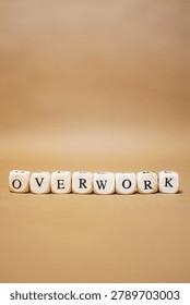 Vertical image of the word OVERWORK made from letter cubes on beige background. Concept of employee burnout, excessive workload, workplace pressure and mental exhaustion.