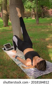 Vertical Image Of A Young Woman Doing Bridge Yoga Pose In City Park In A Summer Sunny Day. Pilates Workout Outdoor 2021. 