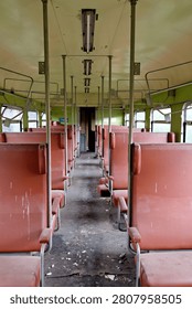 Vertical interior photograph looking down the center aisle of a weathered, abandoned railway passenger car with vintage brown seating.
