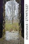 Vertical interior view through dark stone archway looking at bare spring forest