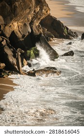 Vertical landscape of Atlantic ocean waves crashing against tall rocky cliffs on the West Coast of Portugal. Majestic rugged coastline illuminated by warm golden hour sunlight
