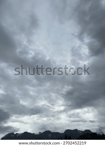 Vertical landscape with dramatic dark storm clouds covering the sky above a misty mountain range.