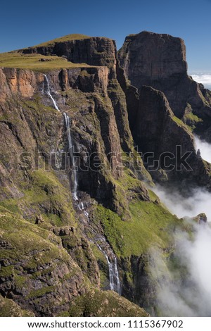 A vertical landscape photograph of the Tugela Falls falling over the escarpment edge in the uKhahlamba Drakensberg Park in South Africa. A cloud iversion sits below and blue sky overhead. Stock photo © 