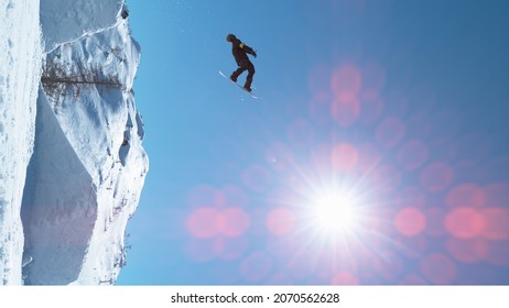 VERTICAL, LENS FLARE: Spectacular Shot Of A Male Snowboarder Jumping High In The Air And Doing A Backflip. Man Snowboarding In Slovenian Mountains Rides Up A Kicker And Does A Backflip On A Sunny Day.