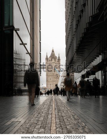 A vertical long exposure shot capturing Tower Bridge in London, UK, framed by modern glass office buildings, with blurred commuters walking rapidly toward the historic landmark.