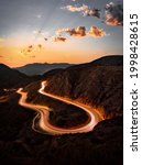 A vertical long exposure shot of a road in the mountains under a sunset sky