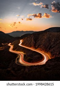 A vertical long exposure shot of a road in the mountains under a sunset sky