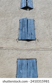 Vertical low angle and close up shot of half closed blue shutters on a stone facade in Beaucaire, Provence, Gard.