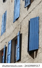 Vertical low angle and close up shot of half closed blue shutters on a stone facade in Beaucaire, Provence, Gard.