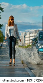 VERTICAL, LOW ANGLE: Unsuspecting Businesswoman Walking Along The Empty Sidewalk Gets Splashed By Careless Driver Driving Down The Empty Road. Car Drives Into Puddle, Splashing Water At Young Woman