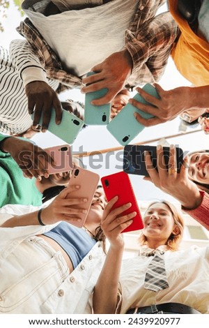Vertical low angle view of a big group of smiling multiracial teenagers addicted to smart phones, watching funny videos, shopping online, enjoying outdoors. Young real people using their cellphones.