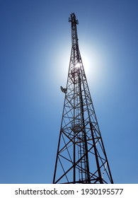 vertical low angle view of cellular or mobile network tower against the sun in the blue sky. - Shutterstock ID 1930195577
