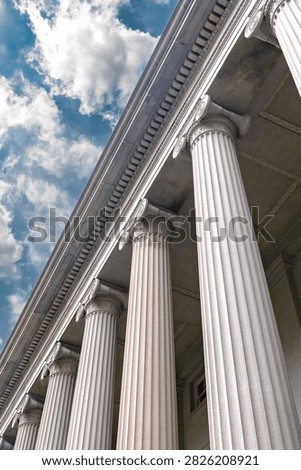 Vertical low angle view follows the Treasury Building Ionic colonnade toward clouds.