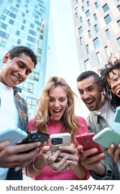 Vertical low angle view of a group of young jaw dropping mixed race people with mobile phones. Excited students using their technological devices. Concept of enterprising, friendly, app, millennial