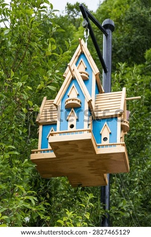 Vertical low angle view of large elaborate wooden Victorian-style birdhouse hung on metal post in summer