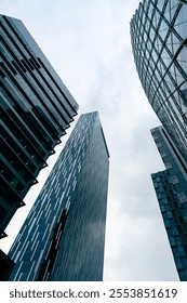 Vertical low angle view of modern glass skyscrapers reaching toward a cloudy sky in a financial district.