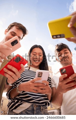 Vertical. Low angle view multiracial group young gen z in circle using phones together outdoors. Cheerful student friends looking at mobile enjoying social media content. People technology addiction 