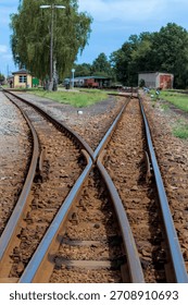 A vertical, low-angle perspective of rusty railway tracks diverging at a switch in a rural train yard. 