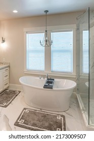 Vertical Luxurious Master Bathroom With Marble Tiles And Window. There Is A Glass Shower Stall With Shower Heads And Shelves Beside The Bathtub With Tray Caddy Near The Double Vanity Sinks