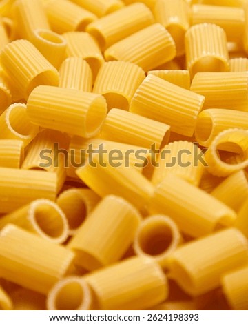 Vertical macro image of dry mezzi rigatoni pasta showing golden-yellow ridged tubes, tightly arranged to highlight their classic cylindrical texture and form