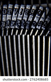 Vertical macro image of old typewriter typebars with metal characters and blurred mechanical parts below.