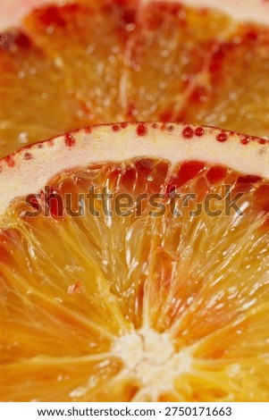 Vertical macro of a sliced blood red Sicilian Cara Cara orange. Sharp focus on the textured rind and adjacent red pulp. Beautiful color gradient from red to yellow. Soft blurry citrus background.