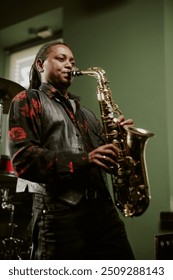 Vertical medium long low angle view of young Black jazz musician playing saxophone on stage