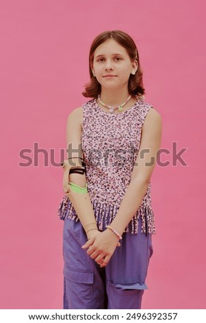 Vertical medium long studio portrait of gen alpha teen girl with prosthetic arm wearing stylish casual clothes posing for camera, pink background