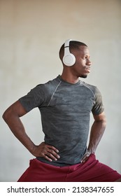 Vertical Medium Portrait Of Handsome Young Black Man Wearing Gray T-shirt And White Headphones Exercising In Loft Room