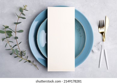 Vertical Menu Card Mockup With Festive Wedding Or Birthday Table Setting With Golden Cutlery, Eucalyptus, Blue Ceramic Plate On Grey Background. Restaurant Menu Concept. Flat Lay, Top View