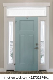 Vertical Mint front door interior with transom window and sidelights. Interior of a house with light gray walls, wooden flooring and a view of two rooms on both sides with windows.