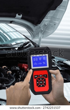 Vertical mobile format image of a handheld car diagnostic scanner analyzing engine system under the open hood of a vehicle. Automotive technician performing vehicle inspection with OBD2 scanner tool in auto repair service center. Ideal for mobile advertising, automotive service promotion, car maintenance apps and digital marketing campaigns.
